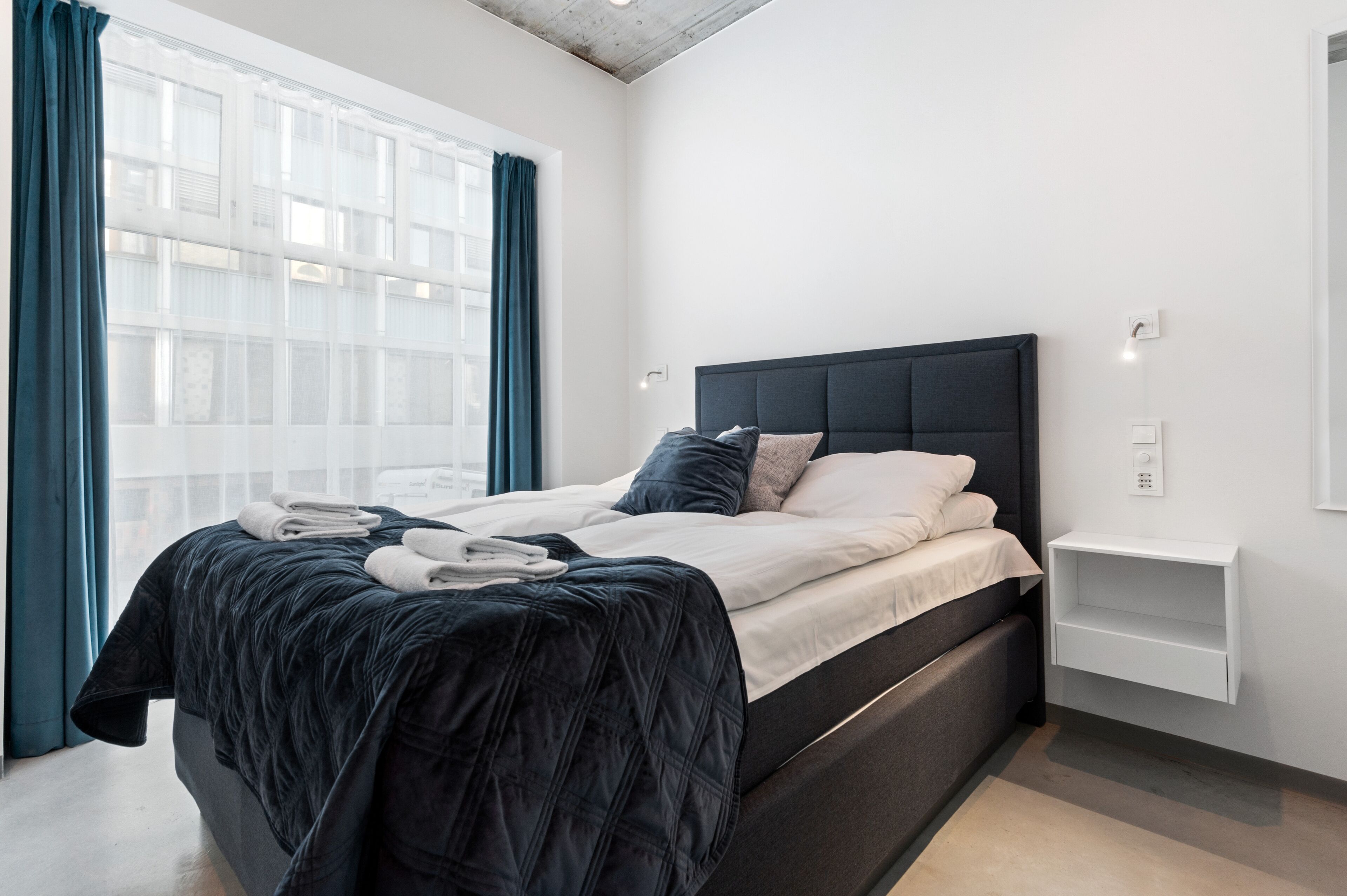 A modern bedroom with a large bed, a bedside table, and a window with curtains.