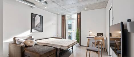 A modern bedroom with a bed, a sofa, a desk, and a TV.
