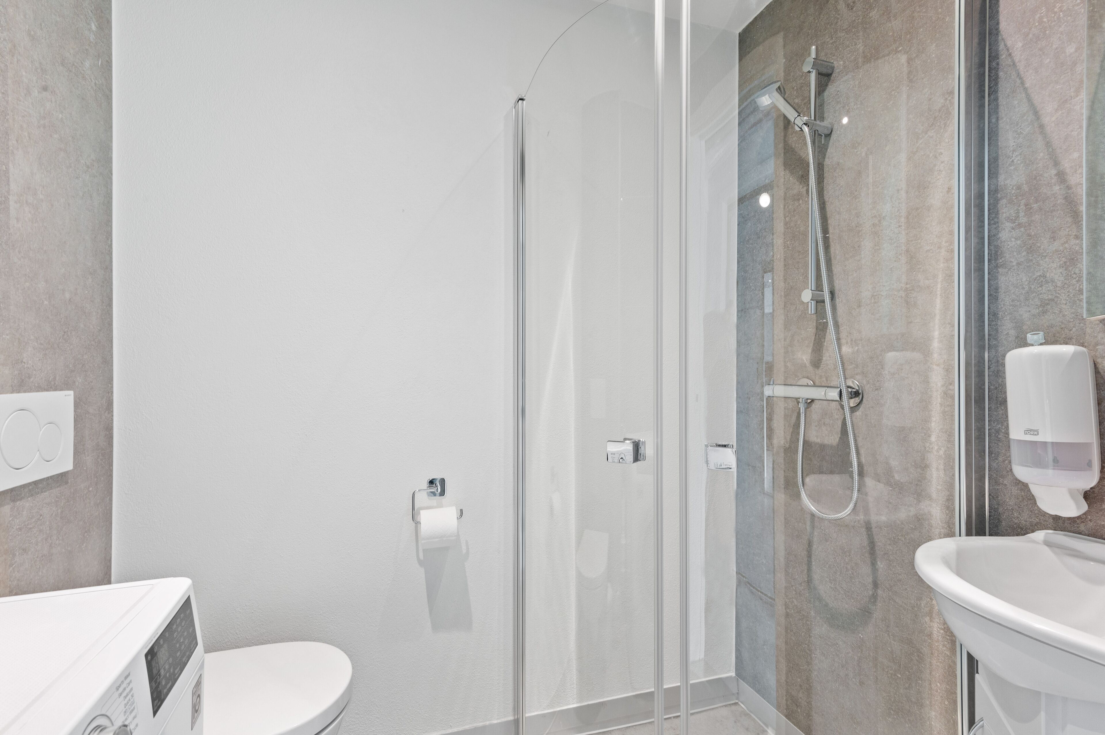 Een moderne badkamer met een glazen douchecabine, toilet en een wastafel met zeepdispenser.