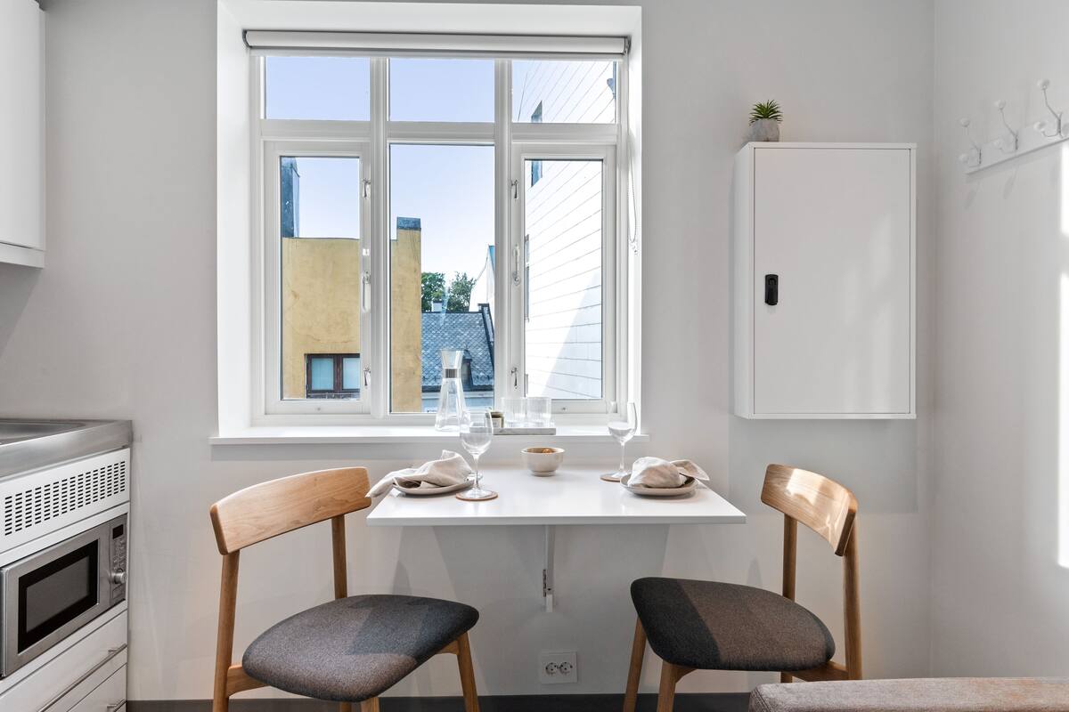 Une cuisine avec une fenêtre, deux chaises, une table et un four à micro-ondes.