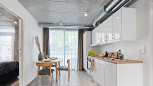 A modern kitchen with white cabinets, a wooden countertop, and a dining area with a table and chairs. - Aalesund City Apartment (Ålesund)