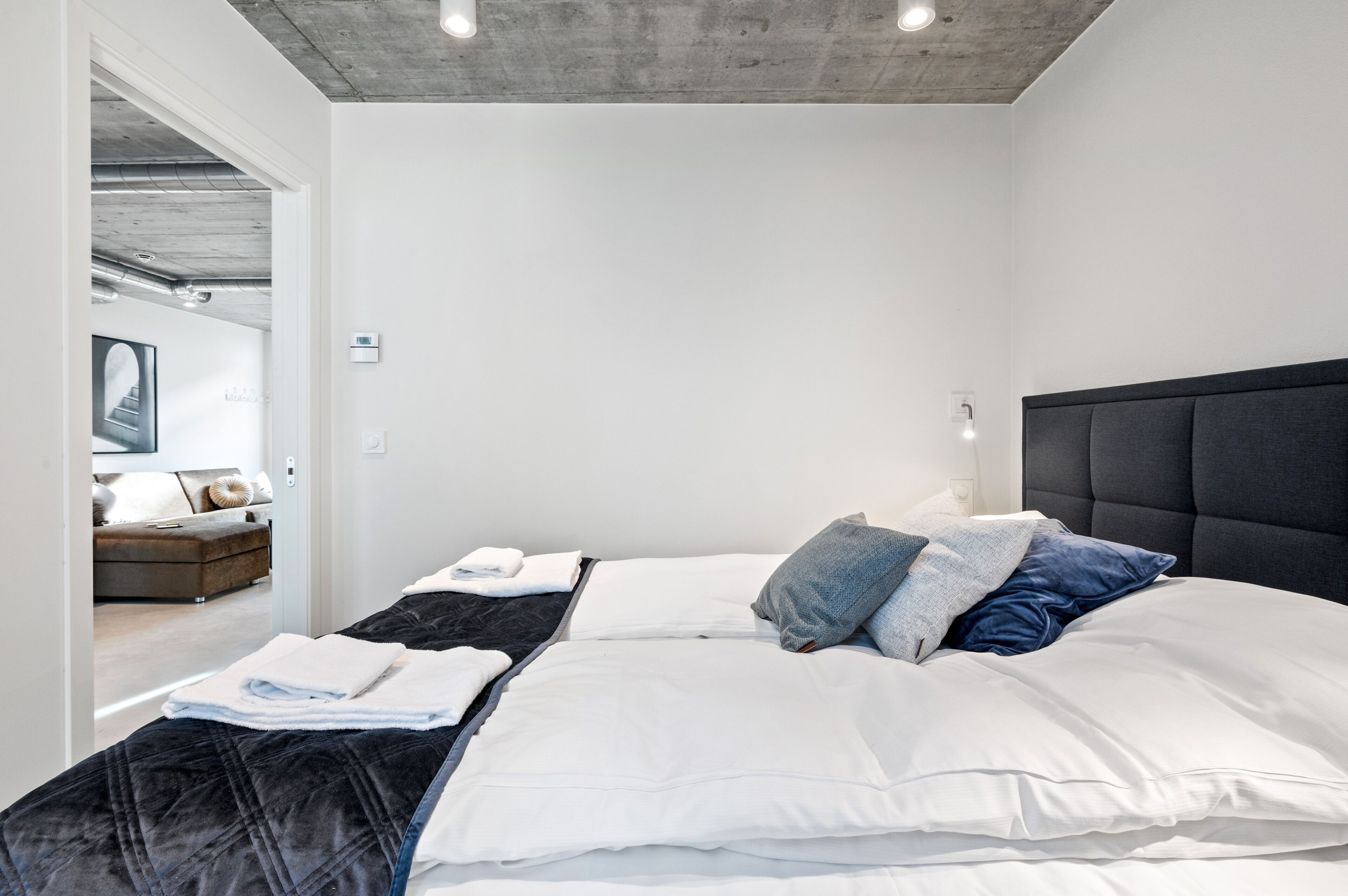Un dormitorio moderno con una cama grande, cabecera y vistas a otra habitación.