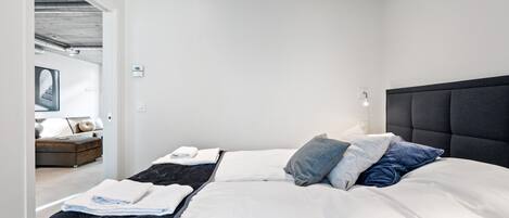 Un dormitorio moderno con una cama grande, cabecera y vistas a otra habitación.