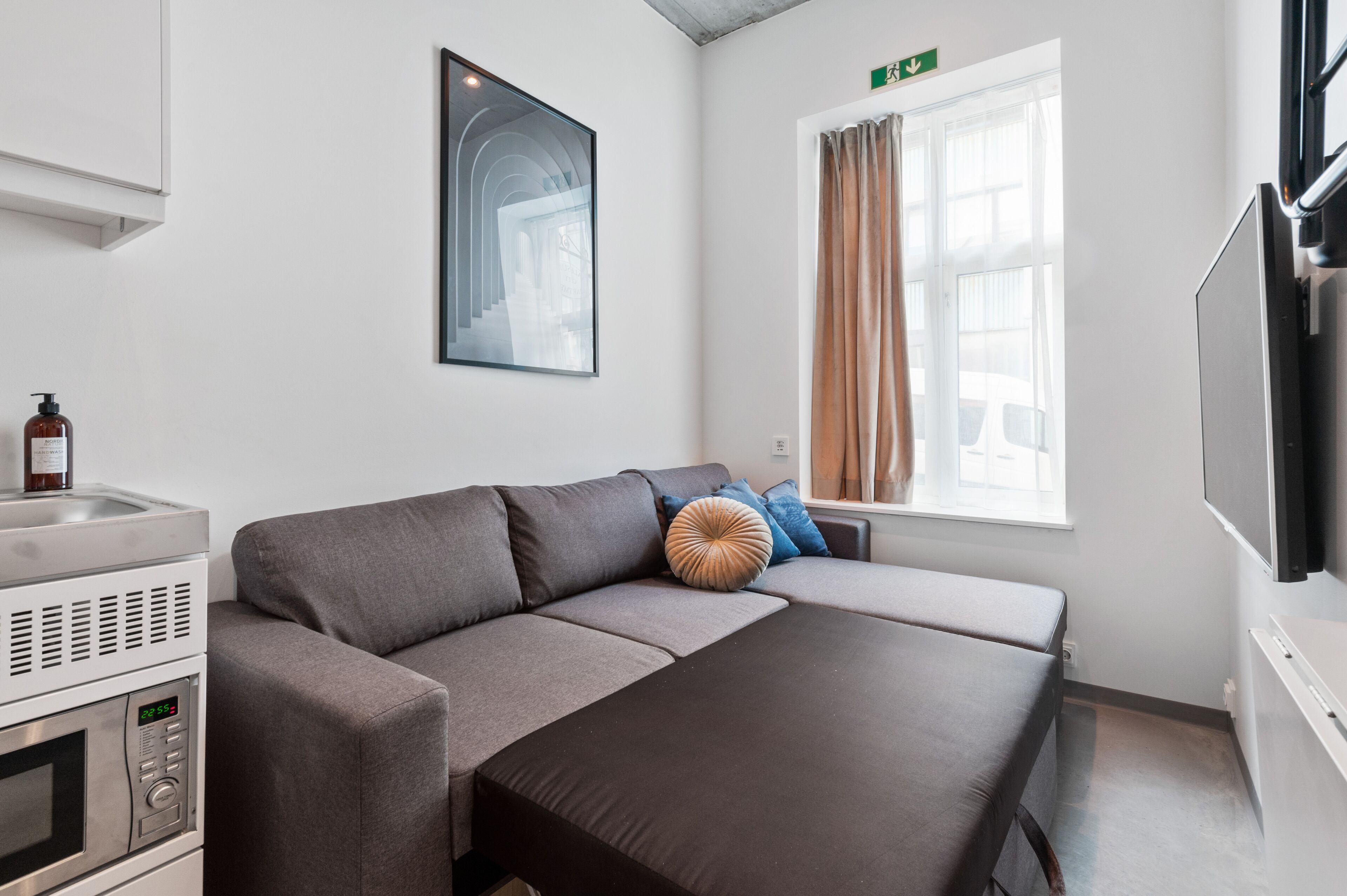 Een moderne hotelkamer met een slaapbank, een televisie, een magnetron en een raam met gordijnen.