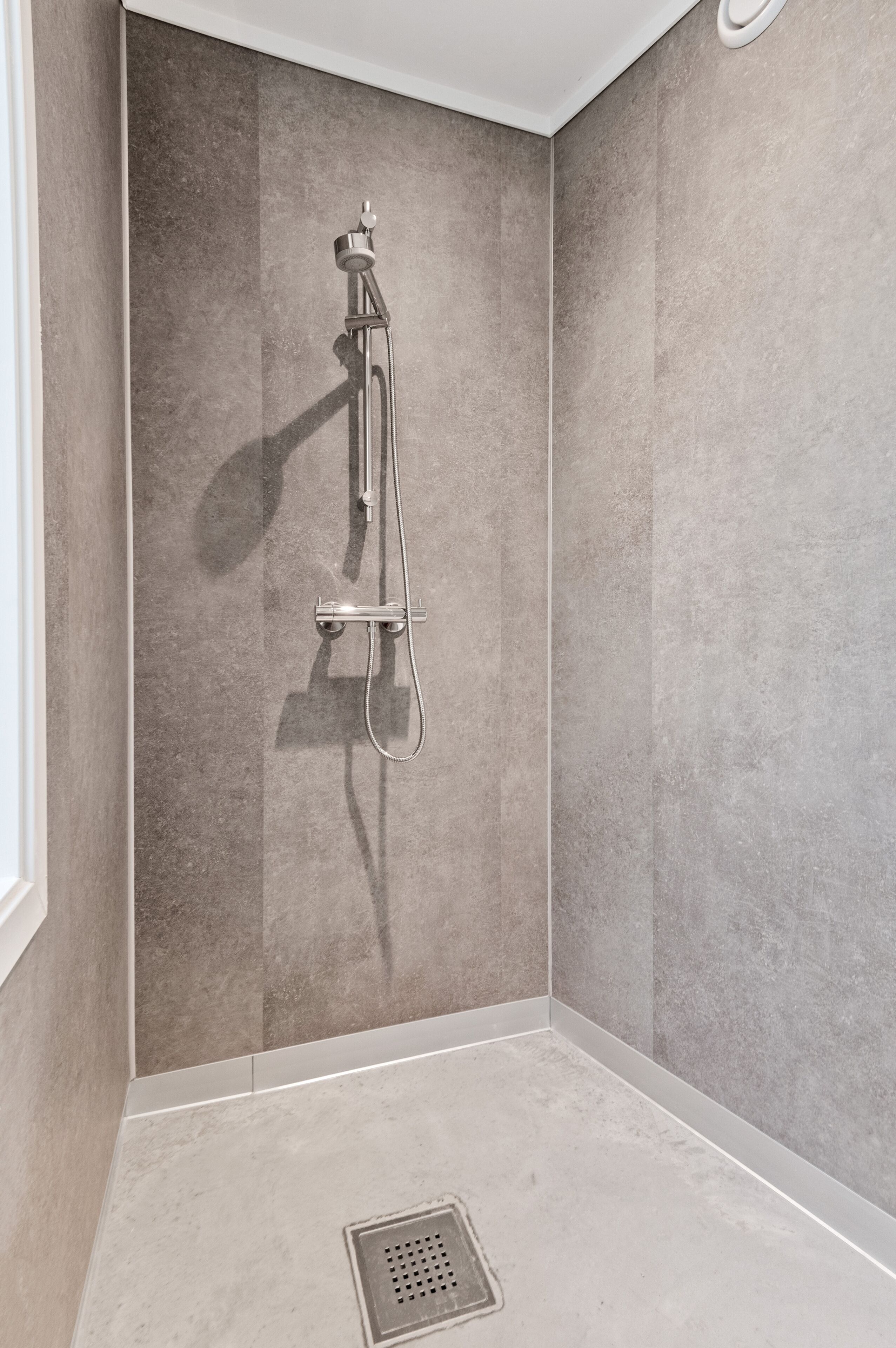 A corner shower with a wall-mounted faucet and a floor drain.