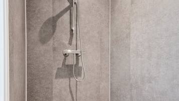 A corner shower with a wall-mounted faucet and a floor drain.