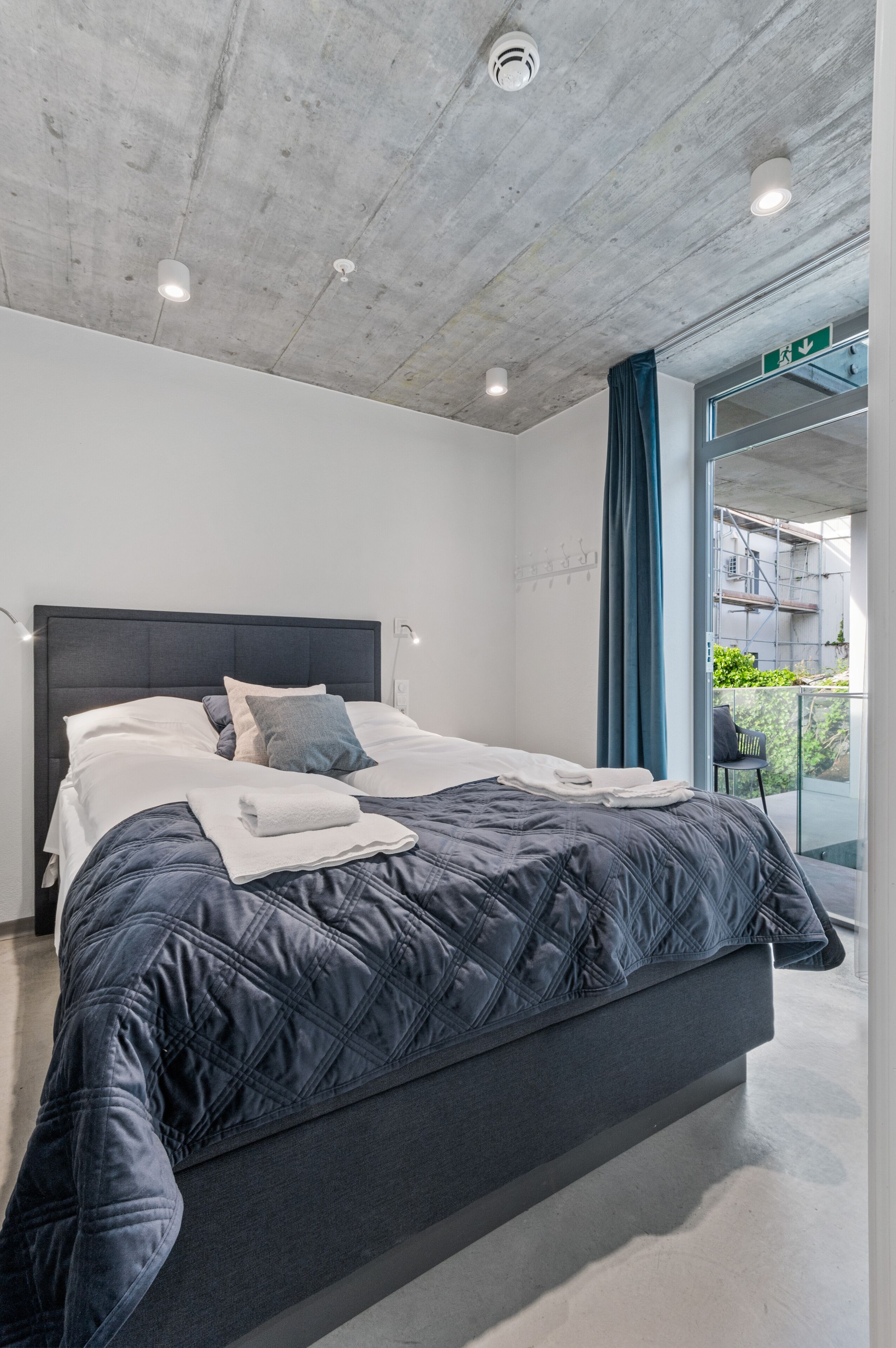 Un dormitorio moderno con una cama grande, techo de hormigón y vistas al exterior.