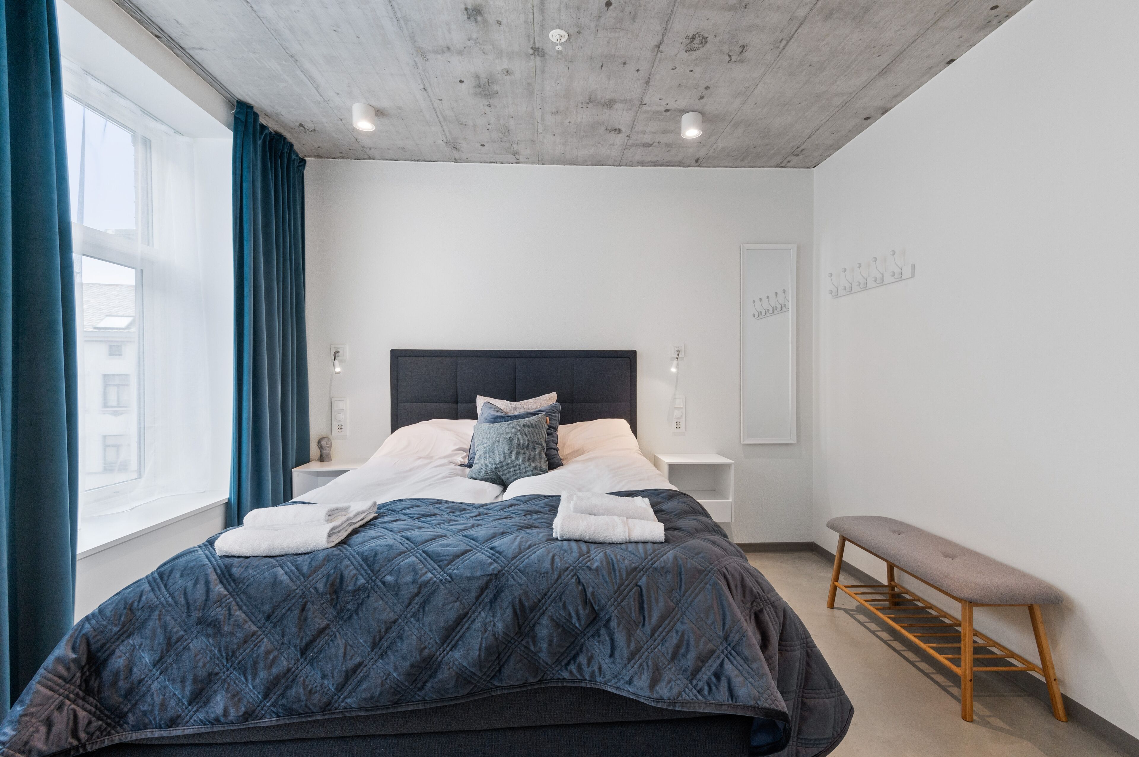 A modern bedroom with a large bed, a bench, and a view of the city.