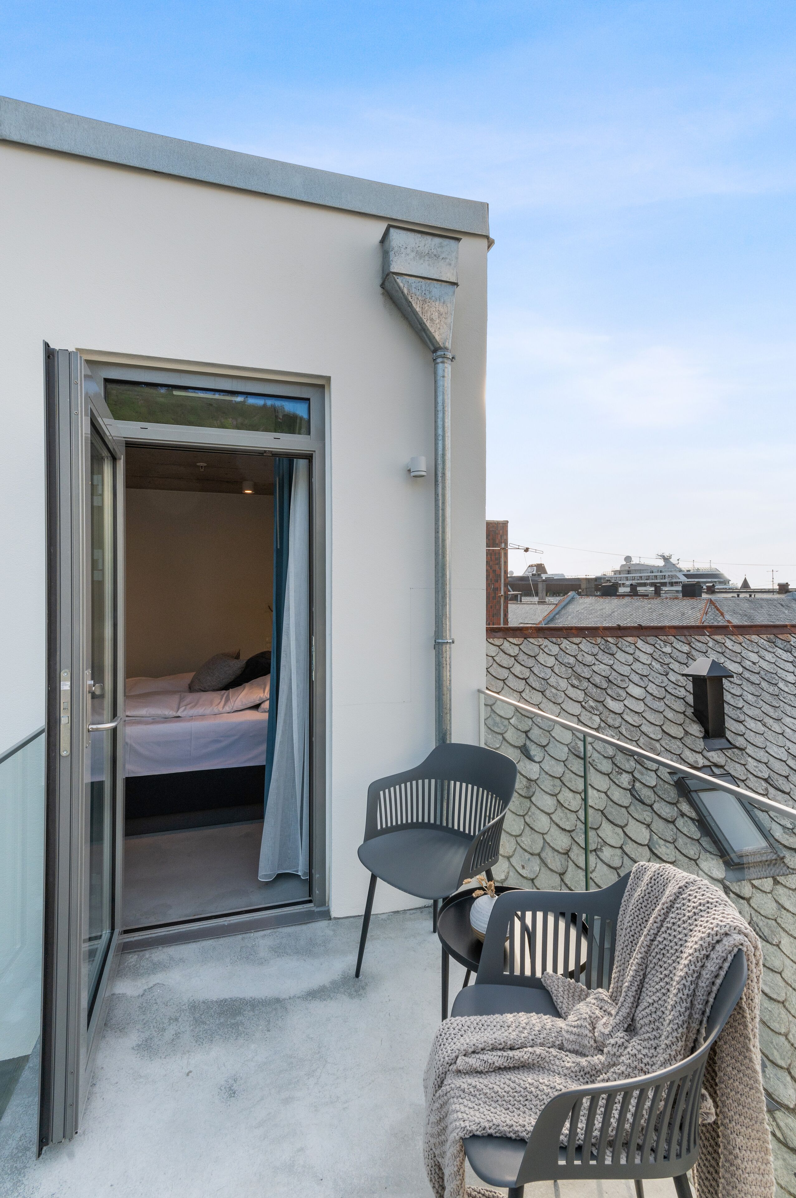 A balcony with a bed, two chairs, and a blanket.