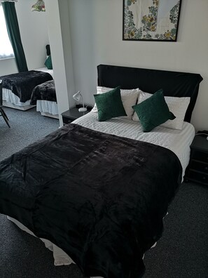 A hotel room with a large bed, a smaller bed, and a desk with a lamp. - Havering Hotel (Romford)