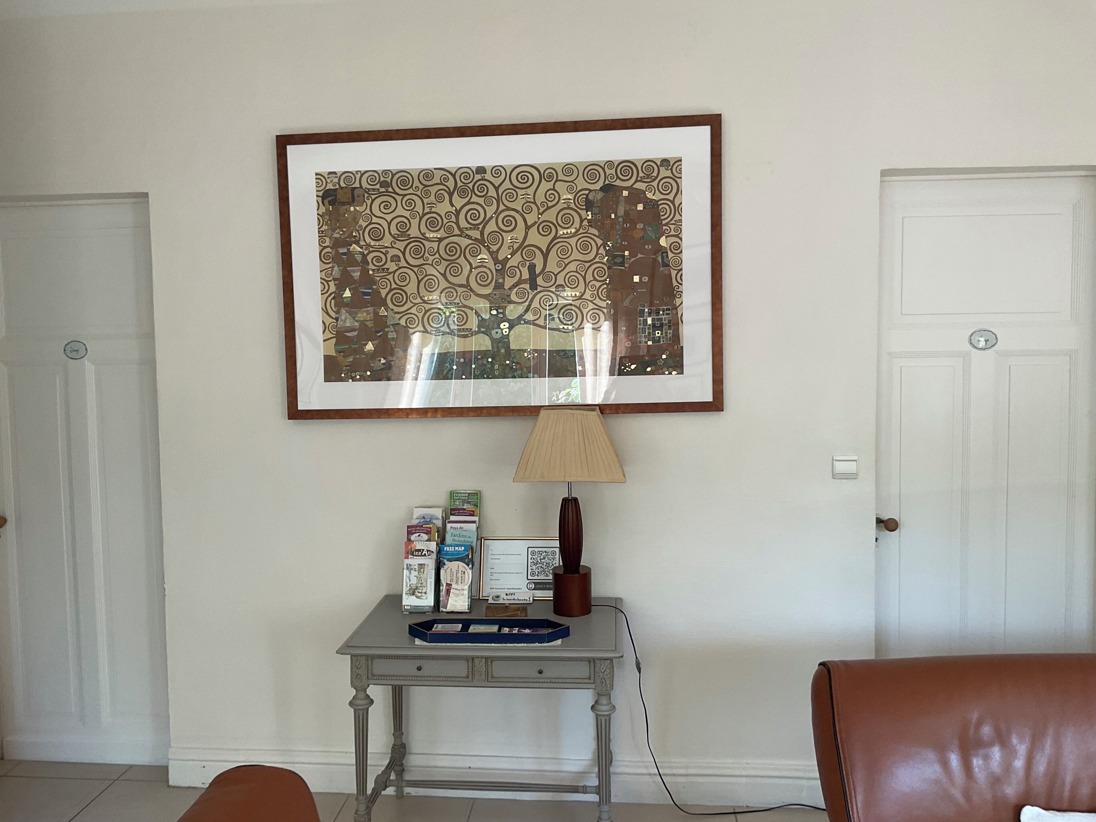 Une pièce comprenant une œuvre d’art abstraite encadrée, une petite table avec des livres et une lampe, ainsi qu’un fauteuil en cuir marron.
