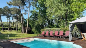 A swimming pool with a wooden deck, surrounded by trees and a covered seating area. - Rural country retreat with private heated pool and driving range! (Verteuil-D'agenais)