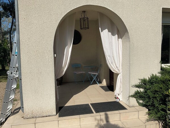 An outdoor patio area with a covered seating space, a small table, and a chair.