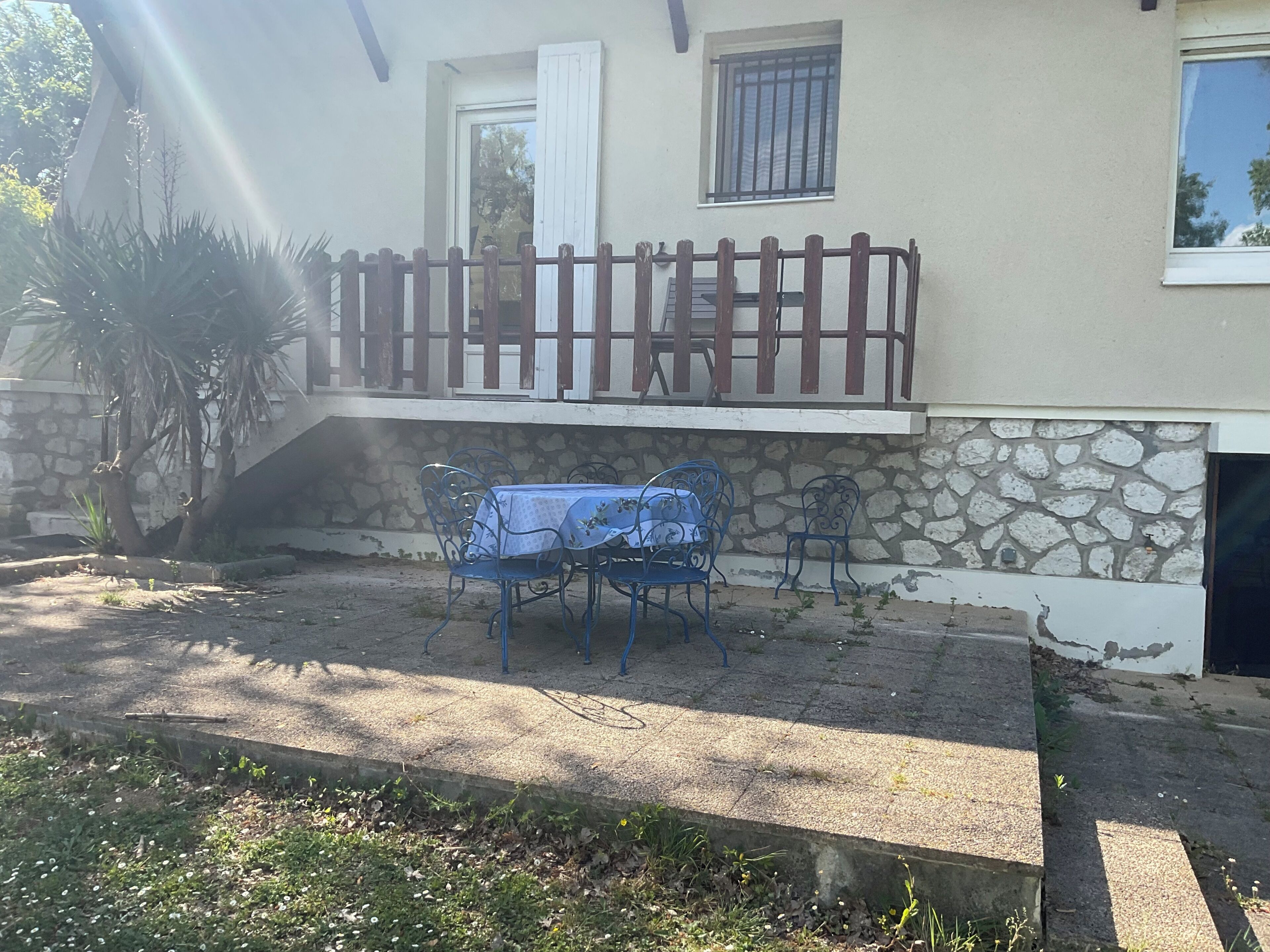 Una casa con pared de piedra, un balcón con barandilla de madera y una mesa con sillas afuera.