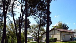 A single-story building with a tiled roof, surrounded by a well-maintained lawn and tall trees. - Rural country retreat with private heated pool and driving range! (Verteuil-D'agenais)