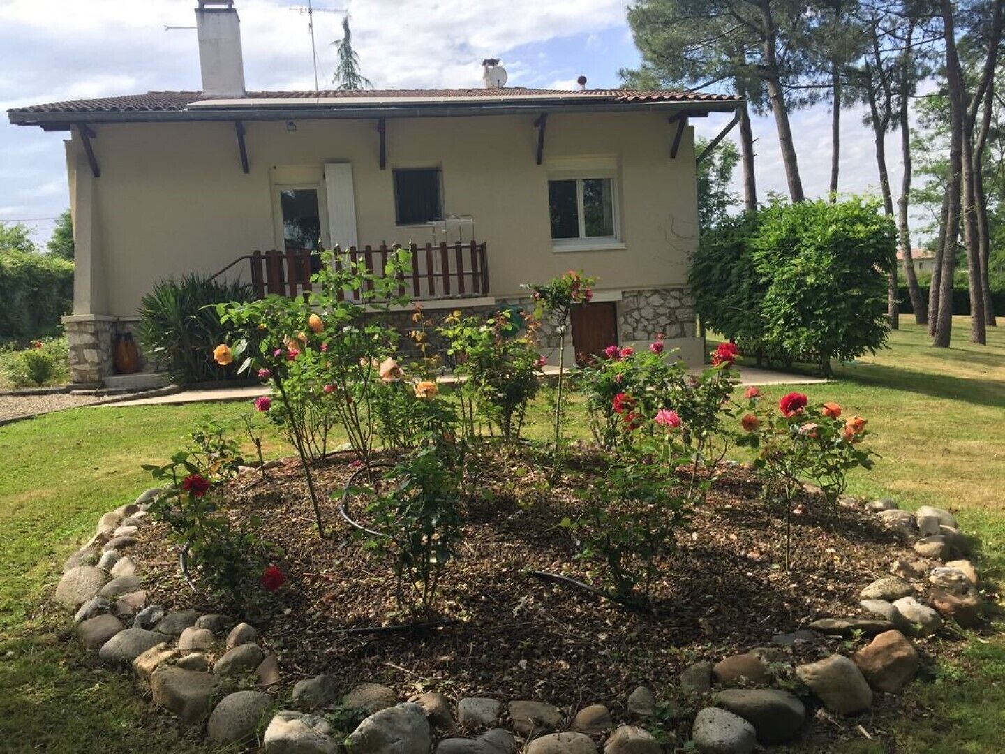A two-story house with a stone facade, a wooden deck, and a garden with roses.