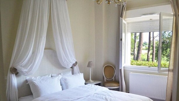 A bedroom with a canopy bed, a chair, a nightstand, and a window with a view of trees. - Rural country retreat with private heated pool and driving range! (Verteuil-D'agenais)