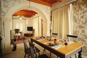 A dining area with a long wooden table set for four, surrounded by stone walls and wooden beams. - Hawk Villa, Timeless Village Escape with Pool (Gerakari, Rethymno)