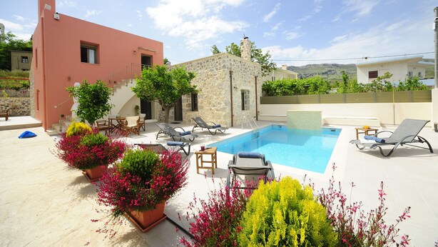 A poolside area with a stone building, a red building, and a white building in the background. - Hawk Villa, Timeless Village Escape with Pool (Gerakari, Rethymno)
