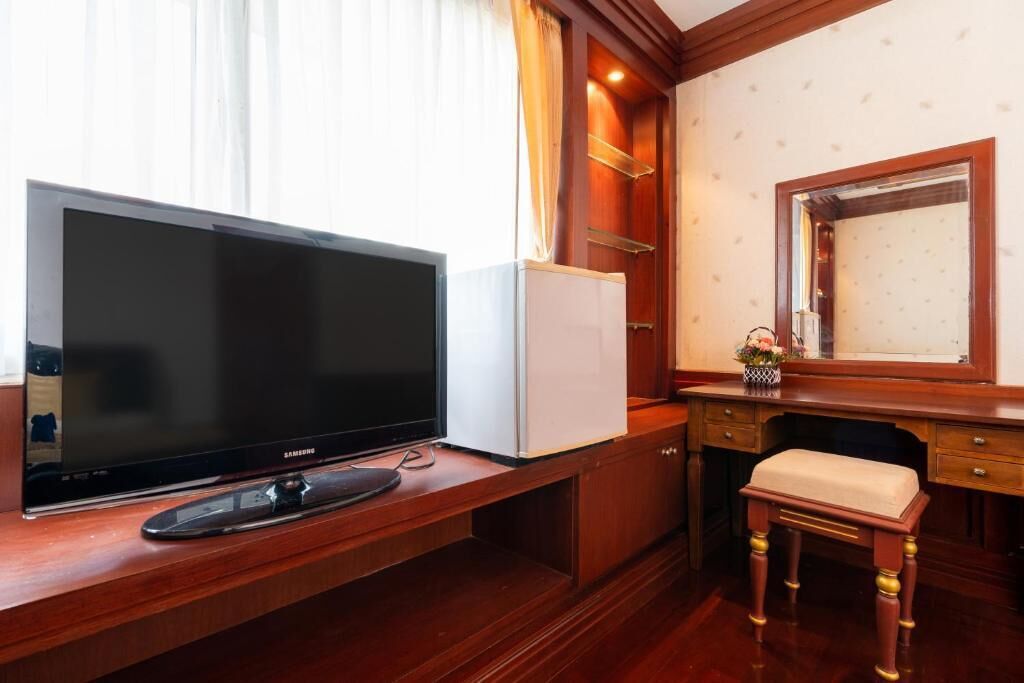 Hotelkamer met een grote flatscreen-tv, een kleine koelkast, een houten bureau, een beklede zitting en een spiegel boven de spiegel.