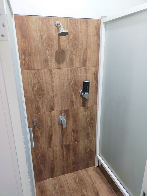 Un área de ducha con pared de paneles de madera, cabezal de ducha de mano y grifo con botón.