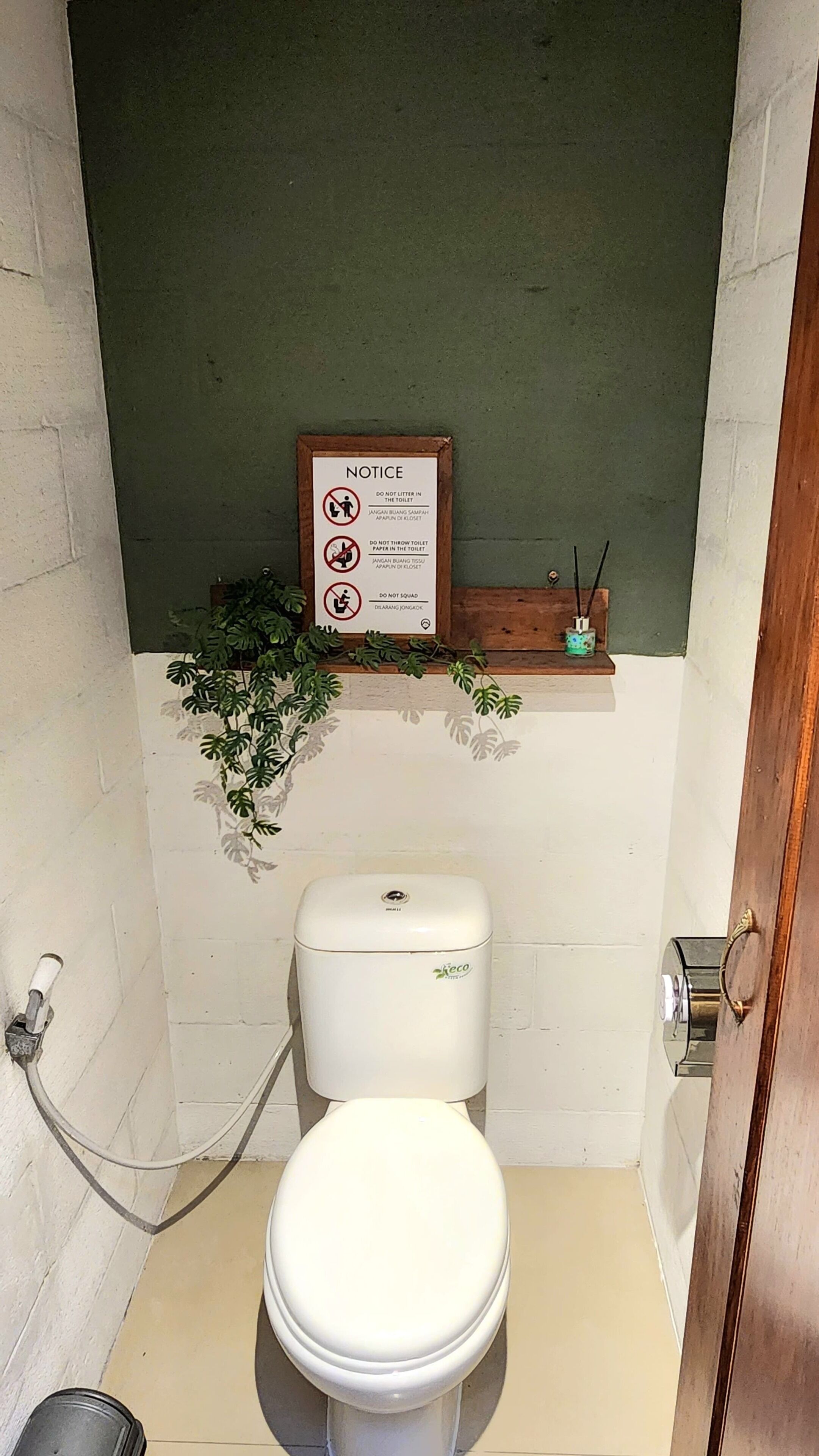 A small bathroom with a white toilet, a notice board with rules, and a green wall.