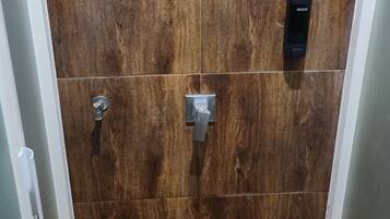 A shower area with a wooden panel wall, a handheld showerhead, and a control panel.