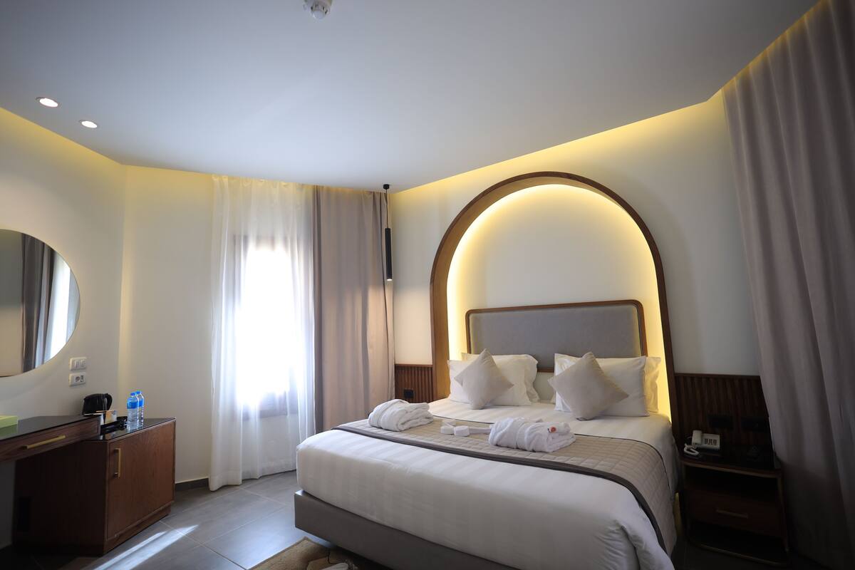 A hotel room with a large bed, a bedside table, a mirror, and a window with curtains.