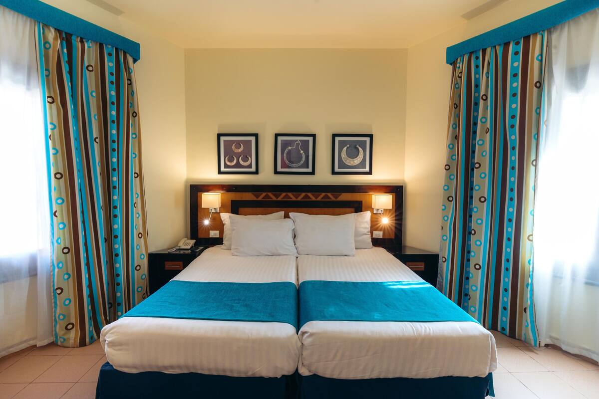 A double bed with two pillows, a nightstand with a phone, and three framed pictures on the wall.