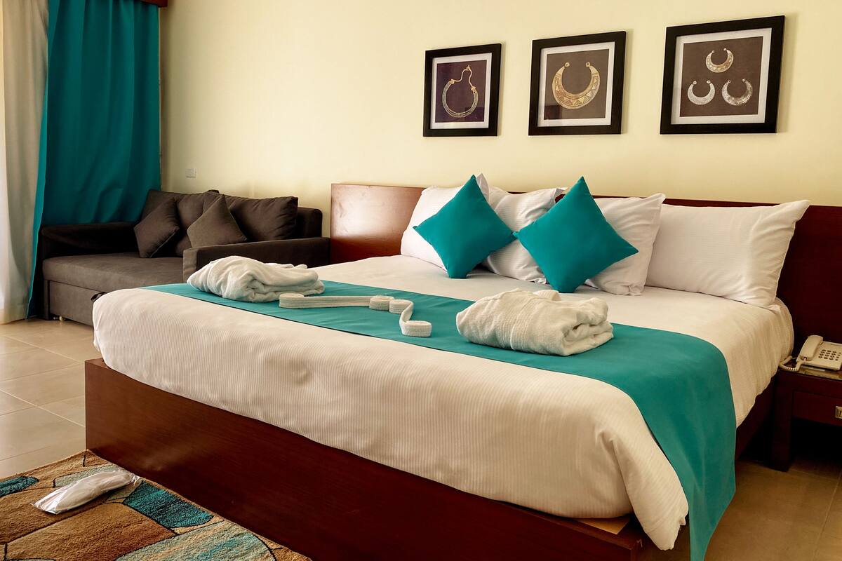 A hotel room with a bed, a sofa, a telephone, and framed artwork on the wall.