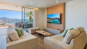 A modern living room with a large TV, comfortable seating, and a view of a marina.