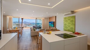 A modern kitchen with a large island, dining area, and a view of the sea.