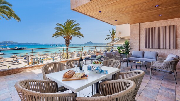 A terrace with wicker furniture, a dining table, and a view of the beach and sea.