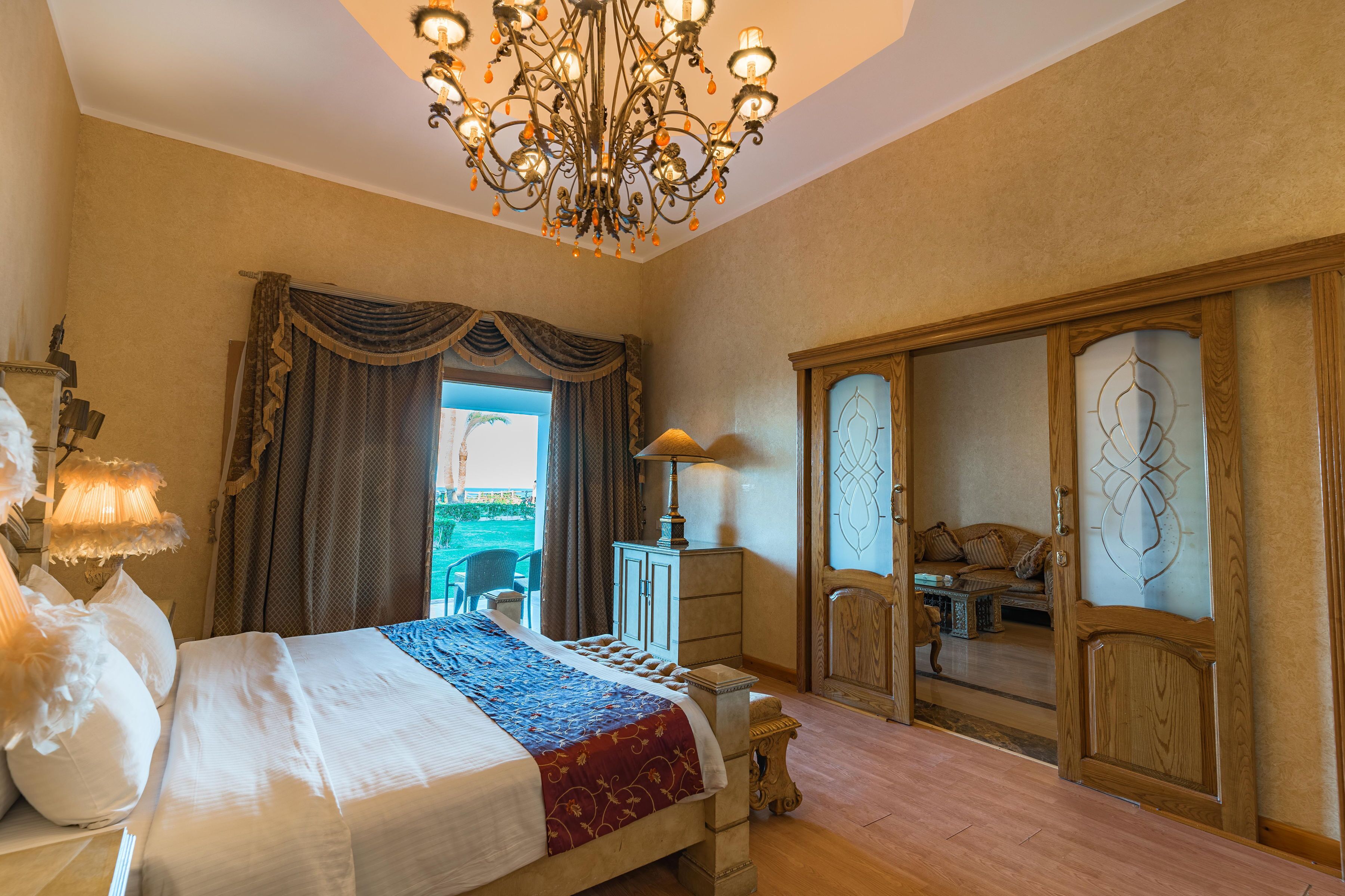 Habitación de hotel con una cama grande, una araña de cristal, un armario de madera y vistas al exterior.