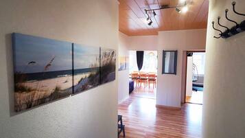 Ein Flur mit einem Gemälde einer Strandansicht, Holzdielenboden und einem Essbereich mit Stühlen und einem Tisch.