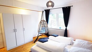 Ein Schlafzimmer mit zwei Betten, einem Kleiderschrank, einem Hängestuhl und einem Fenster mit Vorhängen.