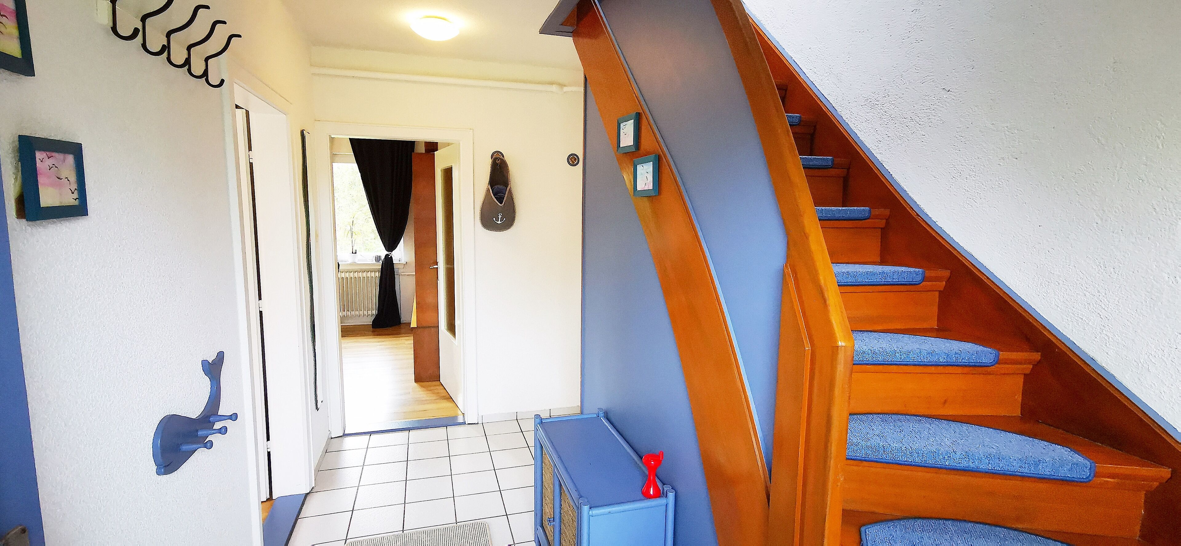 Eine Treppe mit blauen Stufen und einem hölzernen Geländer, die zu einem Raum mit einer weißen Tür und einem Heizkörper führt.