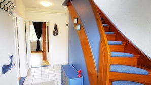 Eine Treppe mit blauen Stufen und einem hölzernen Geländer, die zu einem Raum mit einer weißen Tür und einem Heizkörper führt.