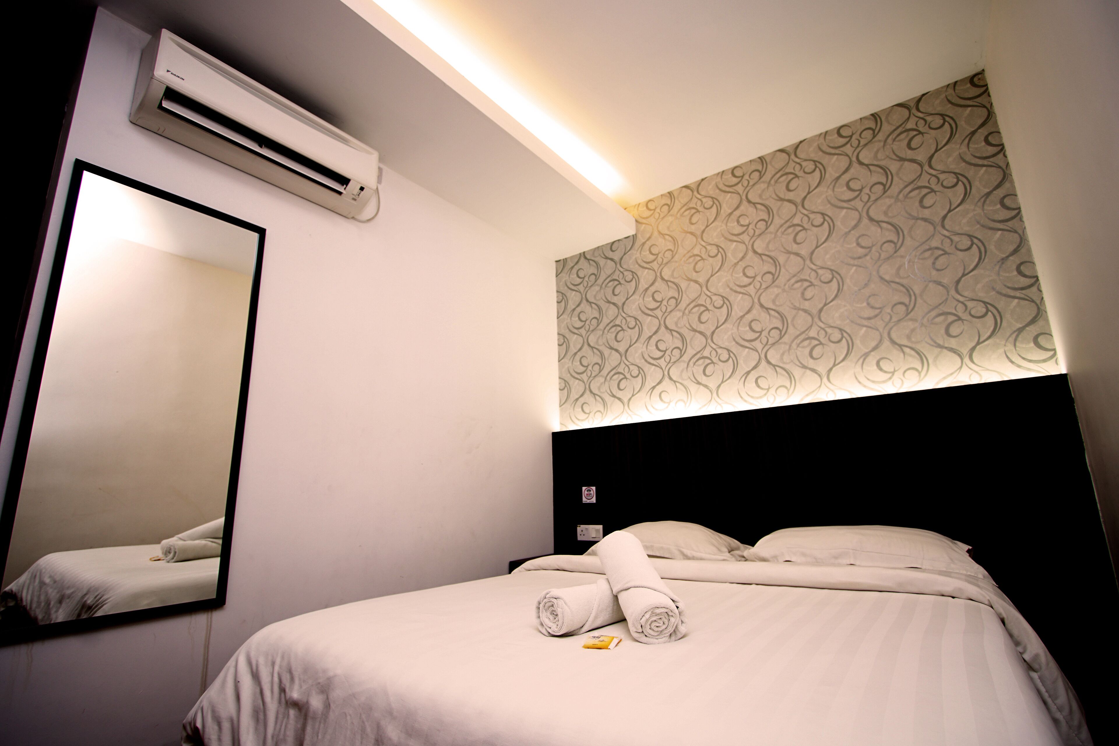 Habitación de hotel con una cama, un espejo grande, aire acondicionado y un papel tapiz estampado.