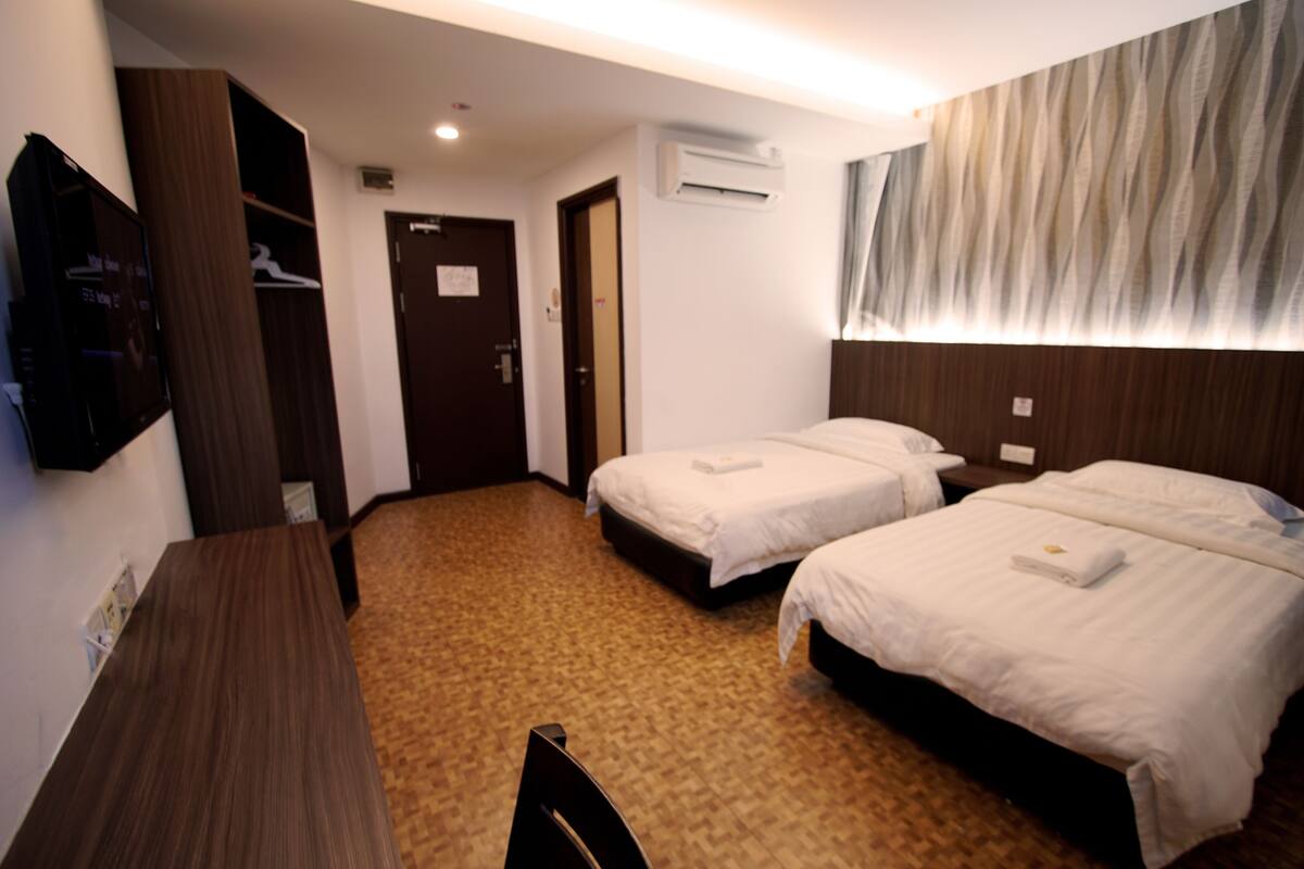 A hotel room with two beds, a wooden desk, a TV, and a wardrobe.