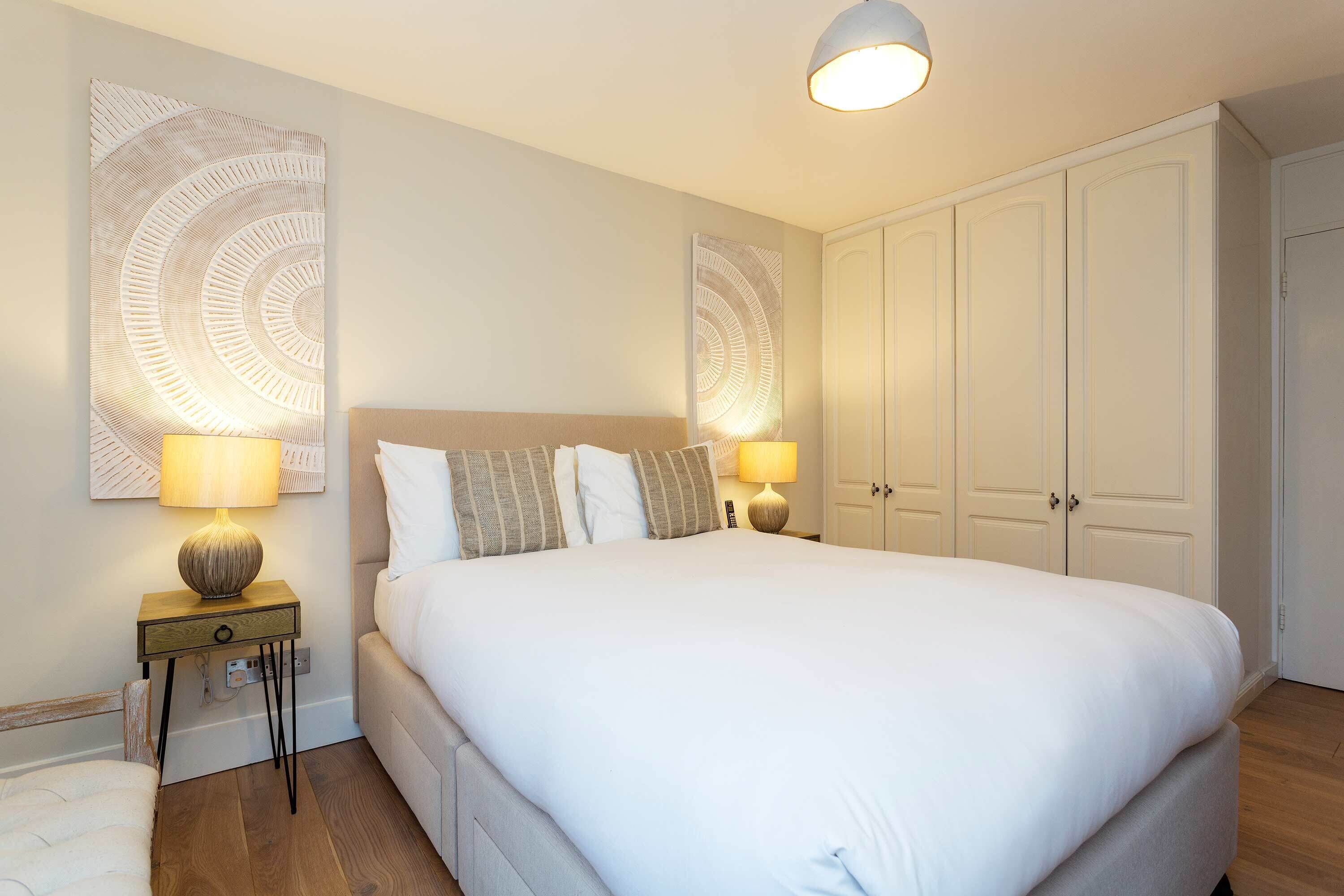 Une chambre à coucher bien rangée, avec un grand lit, deux lampes de chevet, une armoire et une petite table de chevet.