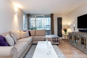 A modern living room with a sectional sofa, a marble coffee table, a TV, and a view of the city through large windows. - Calming Belsize Park Retreat, by Veeve (London)