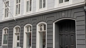 A building with a grey facade, white window frames, and a dark brown door. - PSG 23 - Short Stay Apts by Living Suites (Copenhagen)