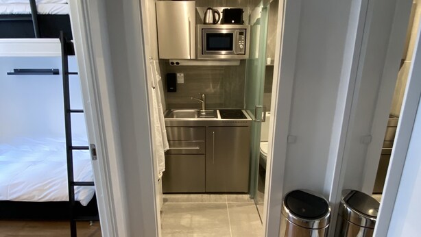 A compact kitchen with a microwave, sink, and stainless steel trash bins. - PSG 23 - Short Stay Apts by Living Suites (Copenhagen)