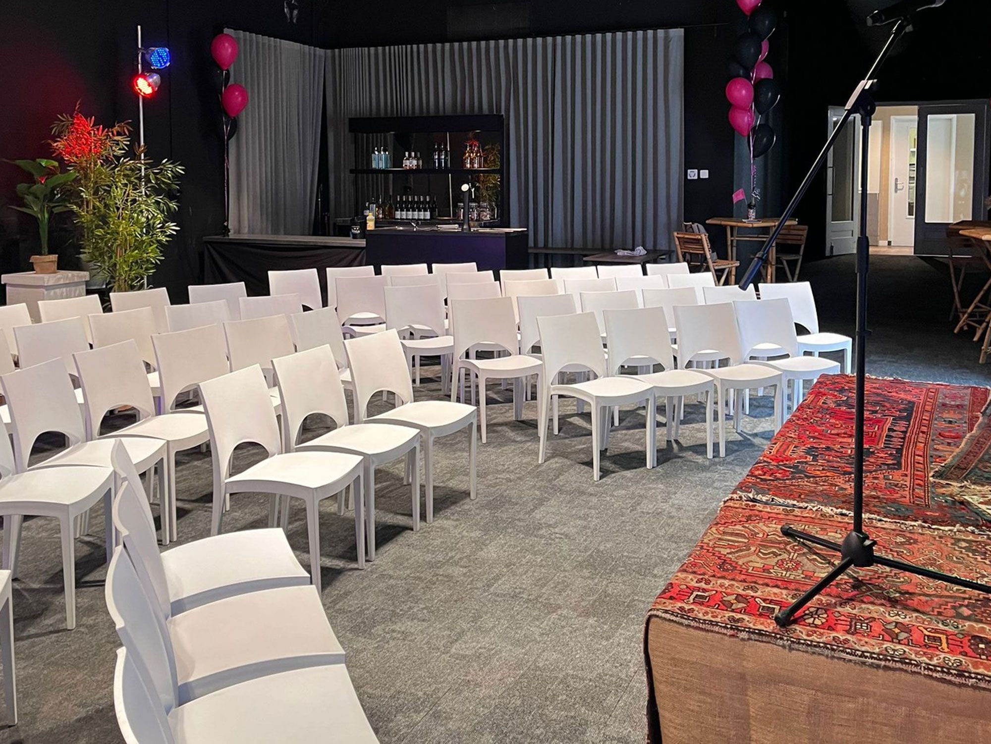 A conference room with rows of white chairs, a stage with a bar, and a patterned carpet.