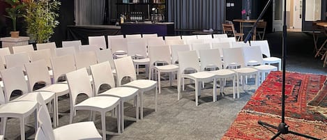 A conference room with rows of white chairs, a stage with a bar, and a patterned carpet.