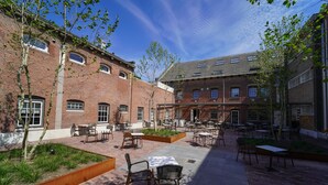 A courtyard with outdoor seating, brick buildings, and trees. - Fletcher Hotel-Restaurant De Oude Gevangenis - Alkmaar (Alkmaar)