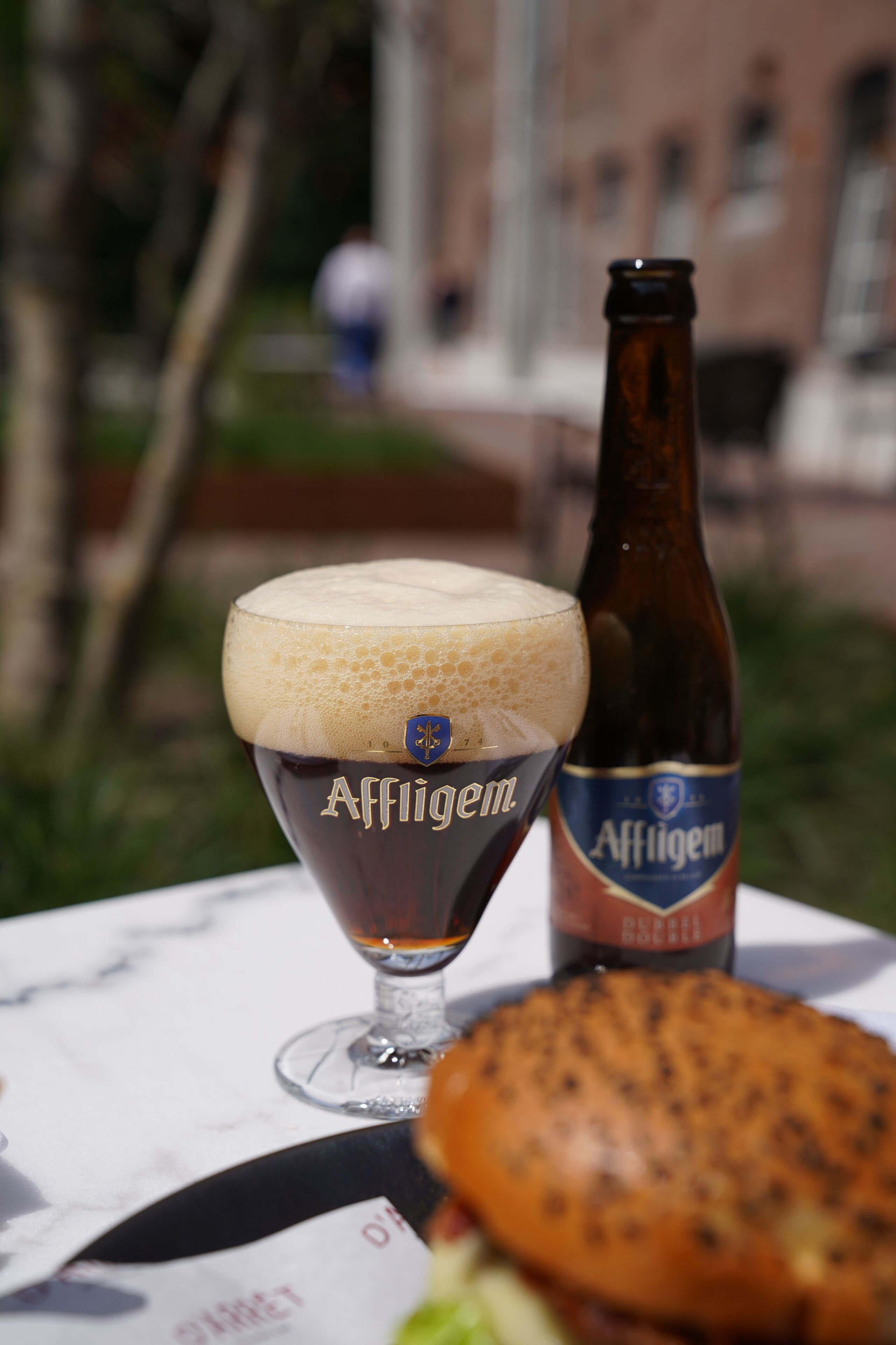 A glass of Affligem beer with a bottle beside it on a table.