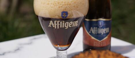Um copo de cerveja Affligem com uma garrafa ao lado, sobre uma mesa.