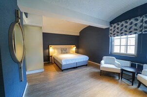 Quarto com cama, mesas de cabeceira, uma cadeira e janela com cortinas estampadas.